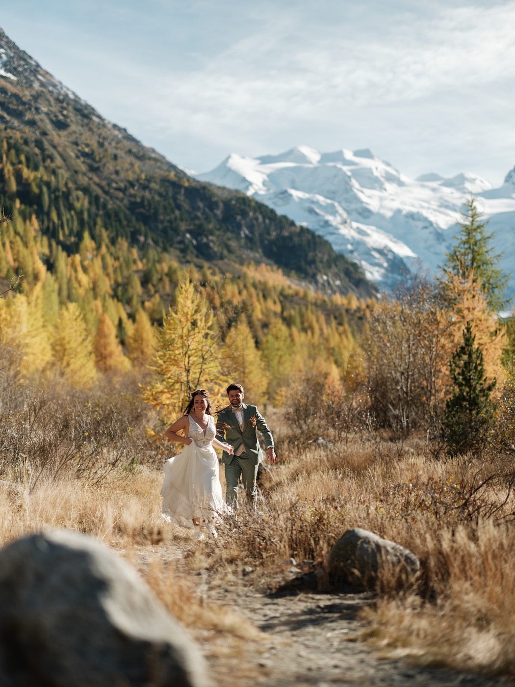 Brautpaar geht über Stock und Stein, lebendige Pose fürs Hochzeitsshooting, Hochzeitsfotograf Graubünden